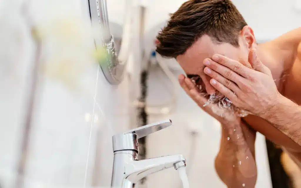 Młody mężczyzna nad umywalką myje twarz w ramach rytyny pielęgnacyjnej