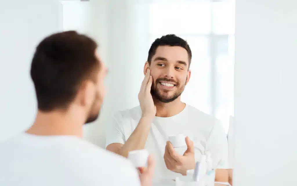 Młody mężczyzna w łazience nakłada krem nawilżający na twarz w ramach rutyny pielęnacyjnej