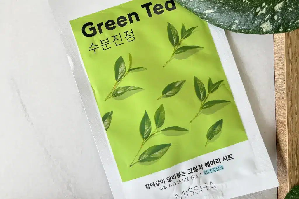 Missha Green Tea maseczka w płachcie nawilżająca leży na stole, w tle zielony liść