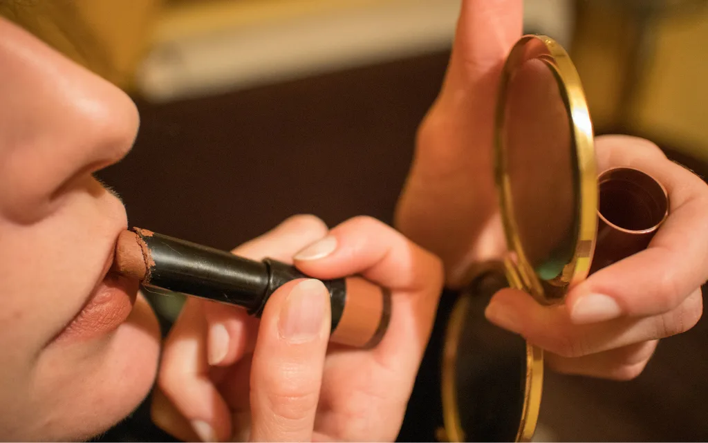 Kobieta przed lusterkiem maluje usta matową szminką