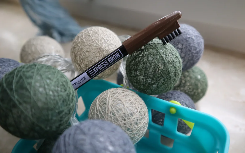 Kredka do brwi Maybelline NY Express Brow Shaping Pencil w niebieskim koszyczku z małymi lampkami w stylu cotton balls