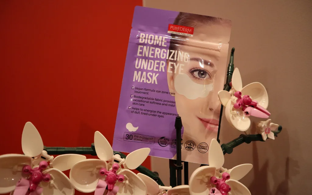 Płatki pod oczy Purederm BIOME Energizing na tle czerwonej ściany i storczyka LEGO