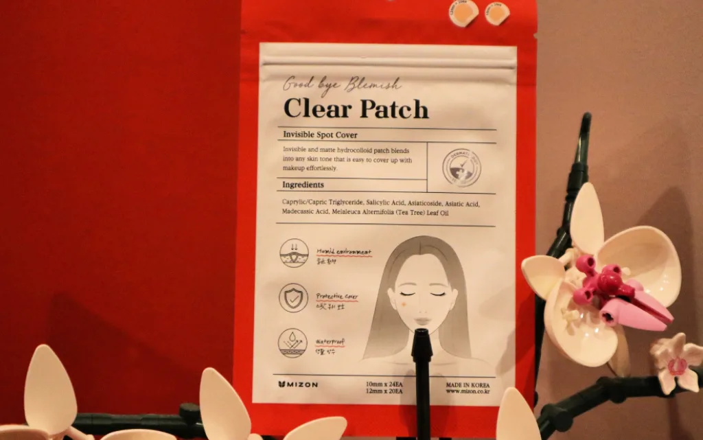 Plasterki na wypryski i niedoskonałości MIZON Good Bye Blemish na tle czerwonej ściany i storczyka LEGO