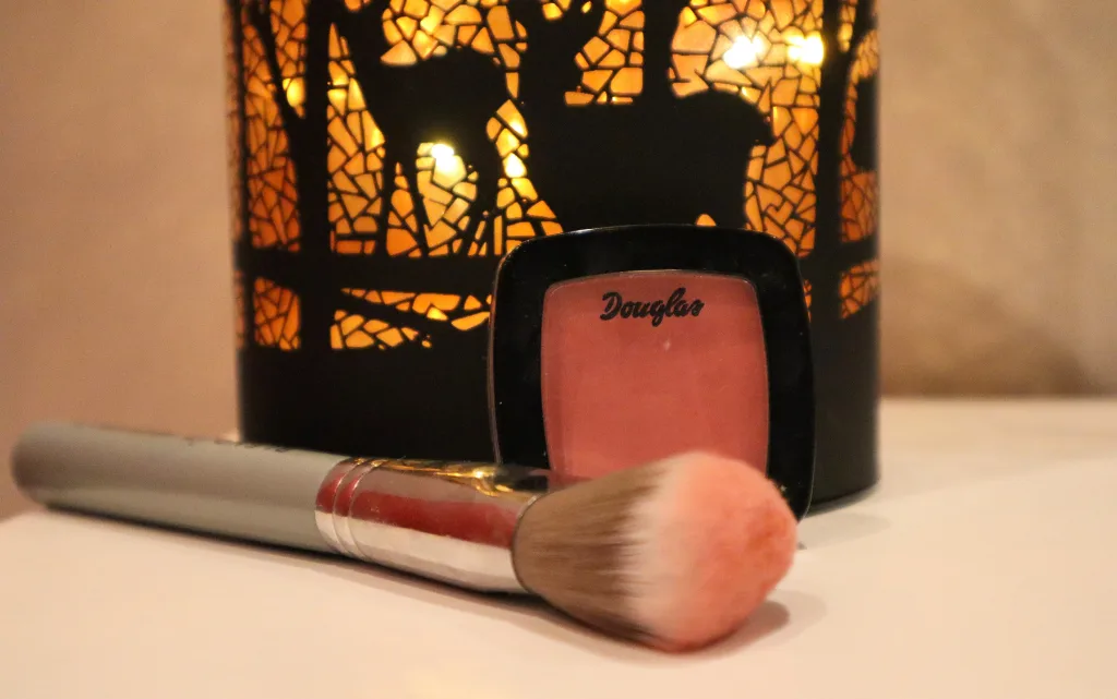 Róż do policzków Douglas Collection Cheek Me Up, pędzel do różu i jesienna lampka w tle