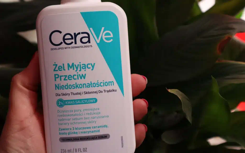 Żel do mycia twarzy przeciw niedoskonałościom CeraVe trzymany w kobiecej dłoni na tle zielonego kwiatka