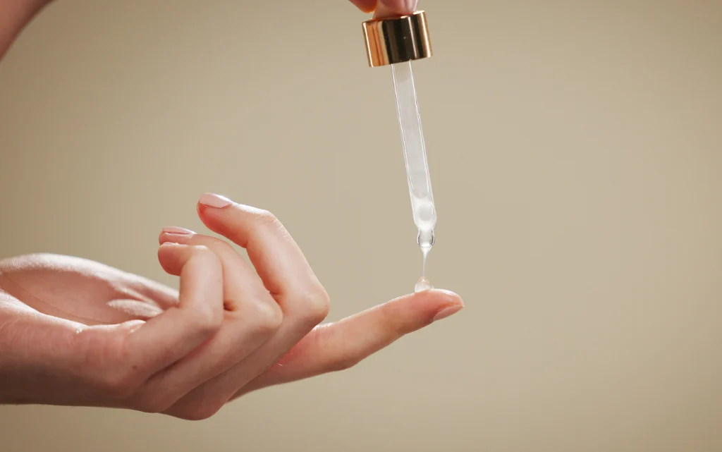 Kobieca dłoń, na której palce nakłada soę serum z retinolem z pipetki
