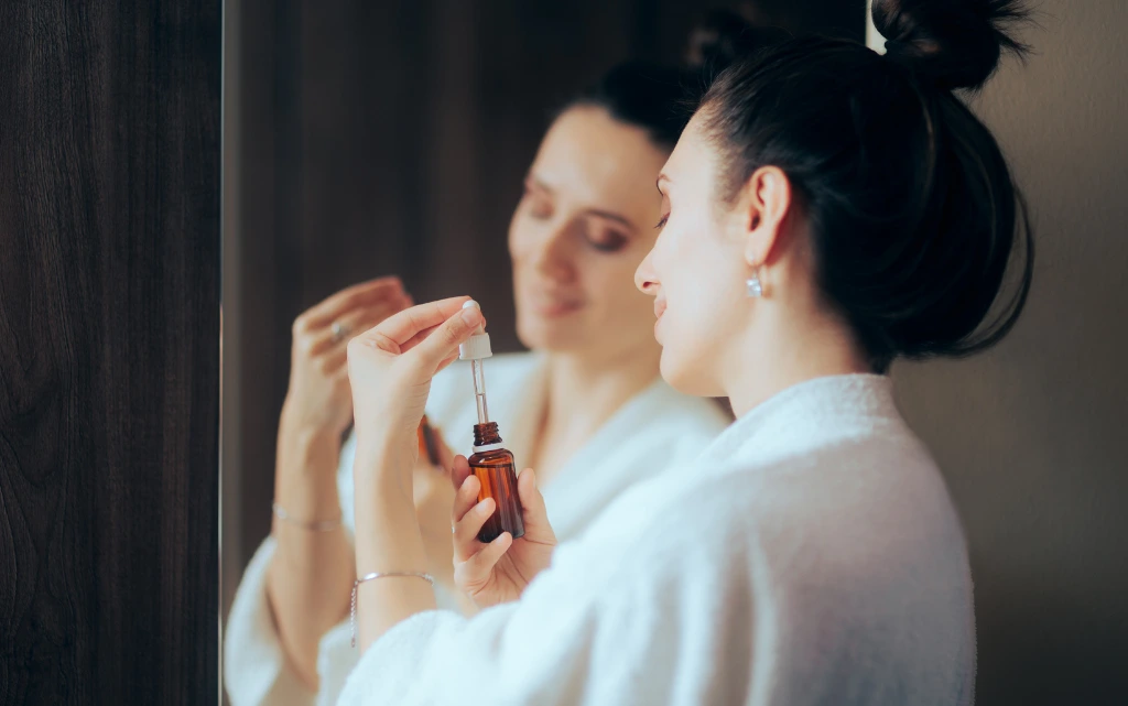 Uśmiechnięta kobieta w szlafroku otwiera serum z retinolem