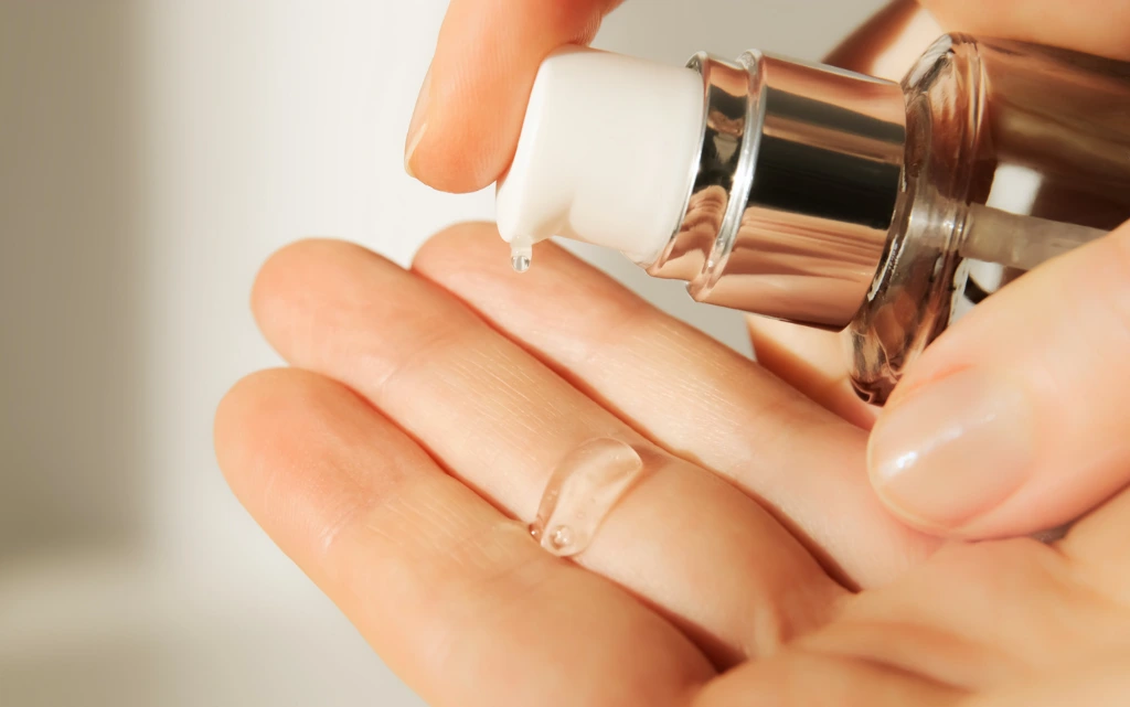Zbliżenie na kobiece dłonie, które nakładają na palce serum z retinolem
