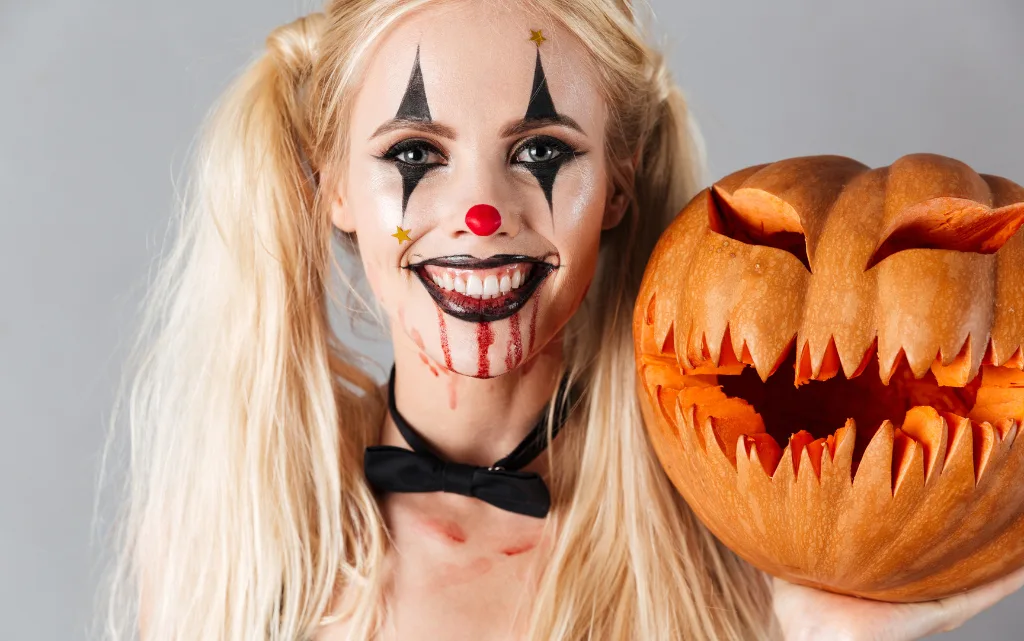 Uśmiechnięta dziewczyna w makijażu na Halloween trzyma wielką dynię