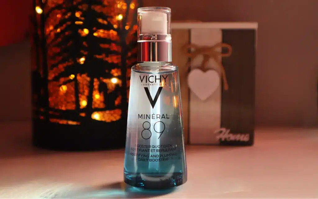 Szklana butelak boostera Vichy Minéral 89 na tle jesiennej lampki i drewnianej dekoracji