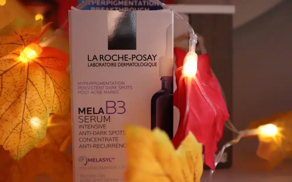 Tekturowe opakowanie serum na przebarwienia La Roche Posay Mela B3 na tle jesiennych lampek