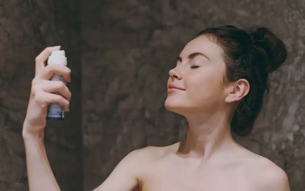 Młoda dziewczyna w łazience używa fixera do wykończenia i utrwalenia makijażu