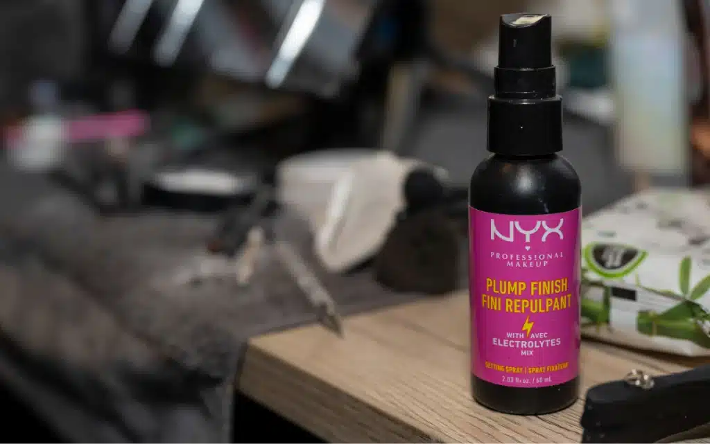 Kosmetyk utrwalający makijaż NYX NY na tle akcesoriów do makiżu