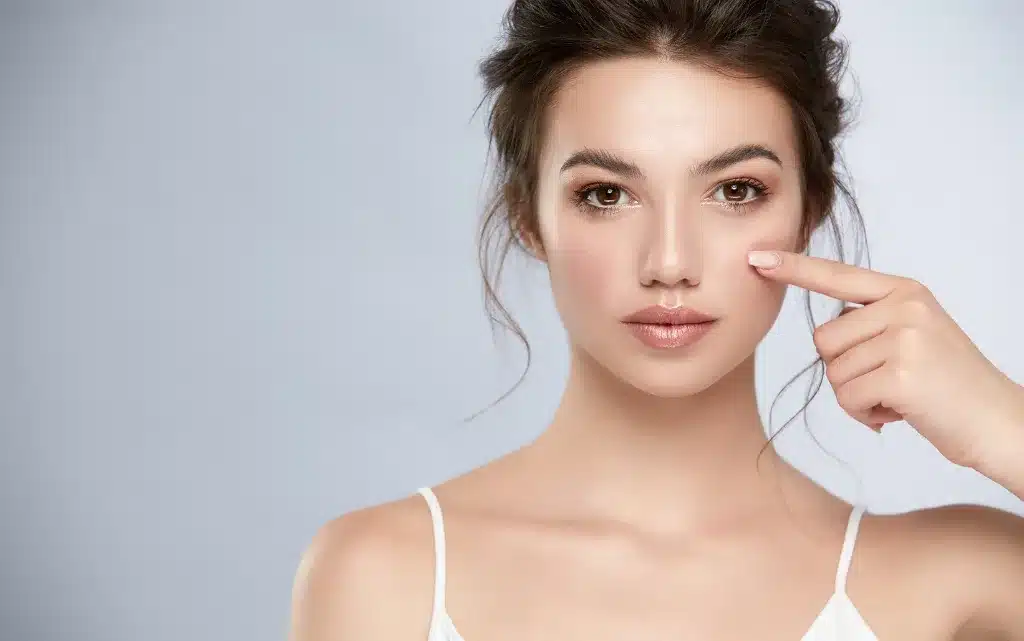 Młoda dziewczyna w lekkim makijażu dziennym trzyma palec wskazujący na policzku