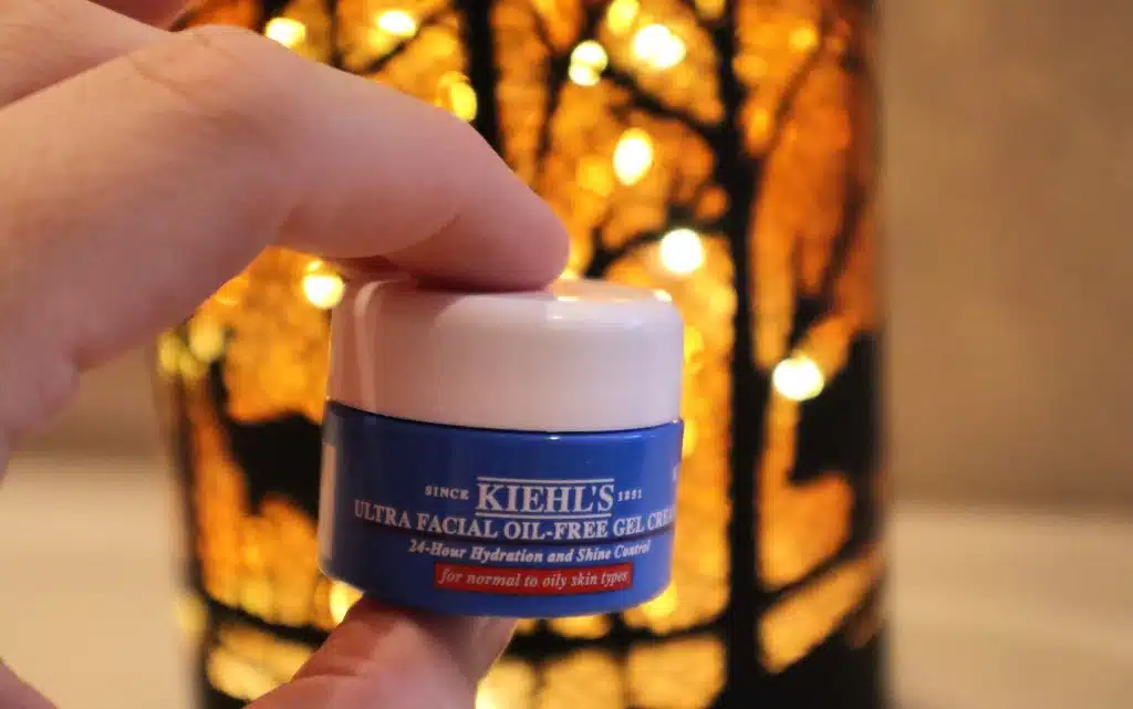 Krem do twarzy tłustej Kiehl’s Ultra Facial Oil Free Gel Cream na tle świecącej dekoracyjnej lampki