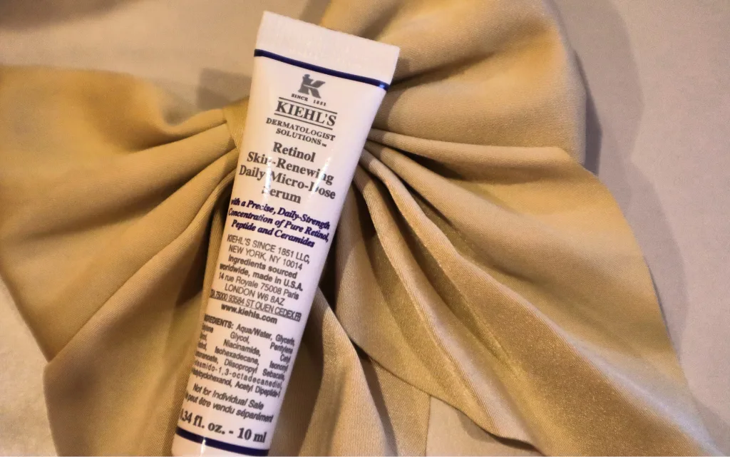 Opakowanie 10 ml serum z retinolem Kiehl’s Retinol Skin-Renewing Daily Micro-Dose Serum na tle jedwabnej kokardy do włosów