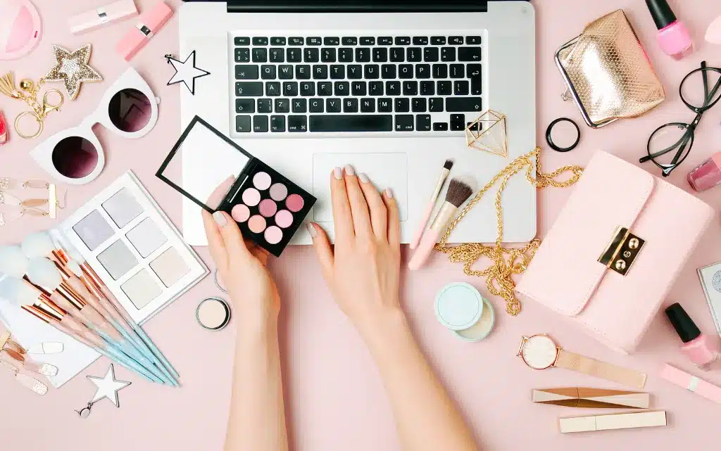 różowe biurko, na nim laptop oraz kosmetyki do zrobienia makijażu biznesowego