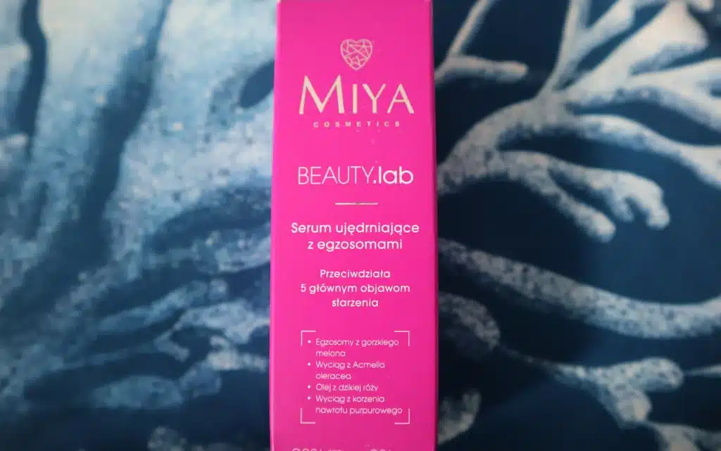 Tekturowe opakowanie serum ujędrniające z egzosomami Miya Cosmetics BEAUTY.lab na tle niebieskiej poduszki