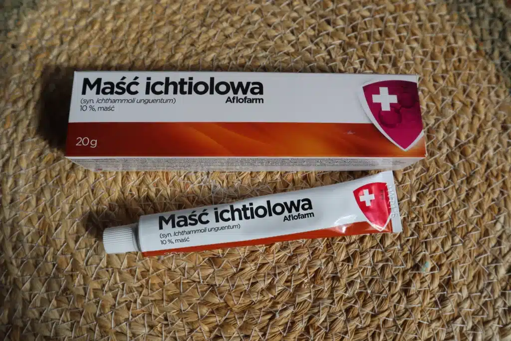 Aluminiowa tubka maści ichtiolowej obok papierowego kartoniku na tle słomianej podkładki