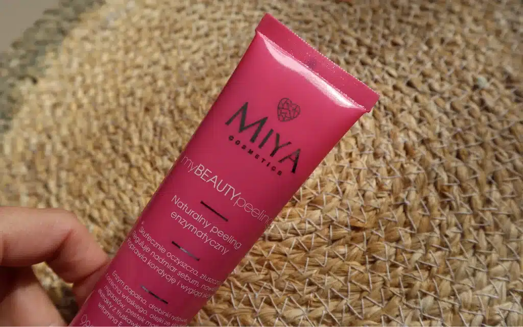 Kobieca dłoń trzyma opakowanie Miya Cosmetics myBEAUTYpeeling naturalny, w tle słomiana dekoracja