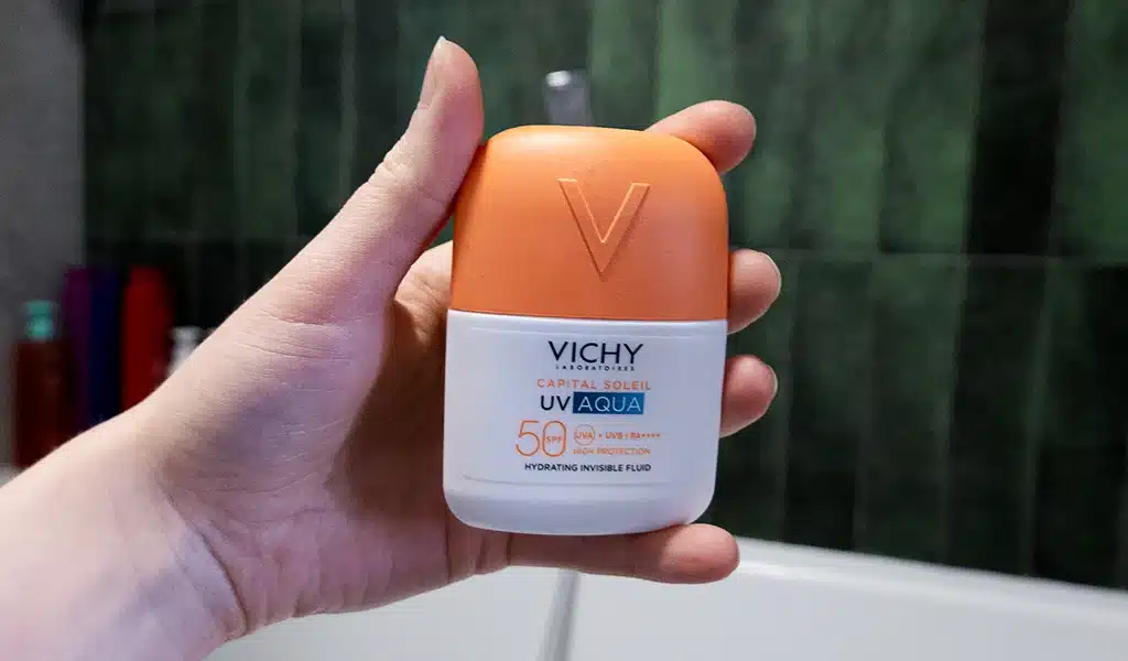 Vichy Capital Soleil UV-Aqua Fluid SPF50 trzymany w kobiecej dłoni, zielone tło