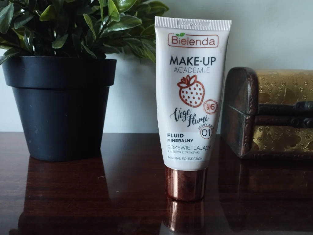 Bielenda Make-Up Academie Vege Flumi Fluid mineralny rozświetlający 01 Jasny Beż na półce obok kwiatka i ozdobnej szkatułki