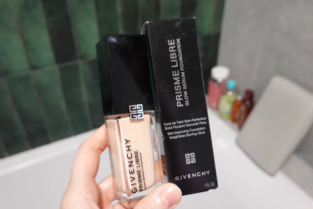 Podkład poprawiający wygląd skóry Givenchy Prisme Libre Glow Serum w kobiecej dłoni, obok papierowy kartonik