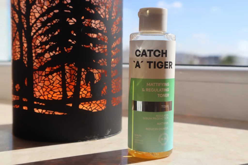 Catch a Tiger Tonik matująco-regulujący na parapecie, obok ozdobna lampka