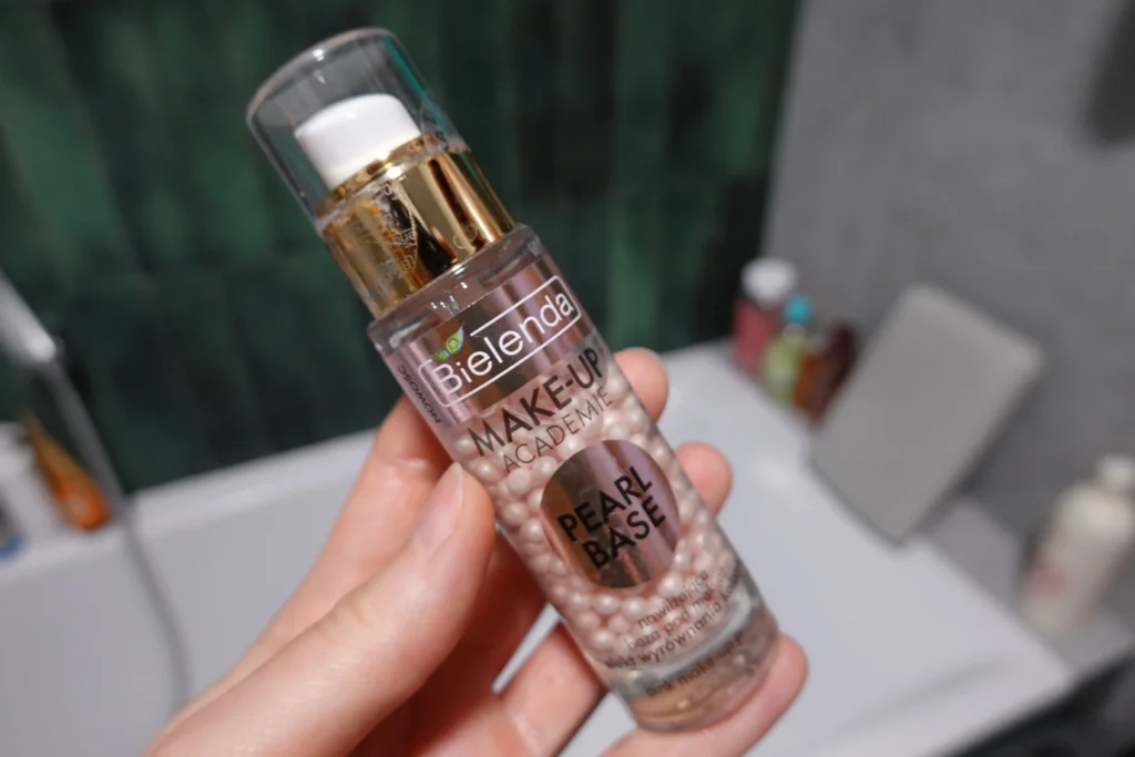 Różowa baza pod makijaż Bielenda Make-Up Academie Pearl Base trzymana w kobiecej dłoni na tle łazienki
