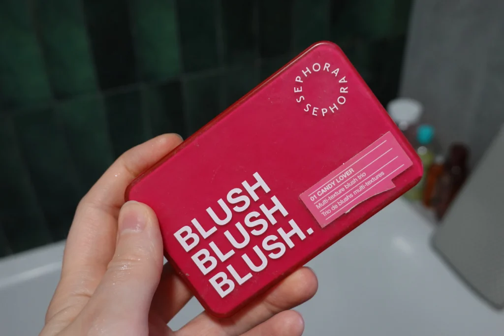 Paleta trzech róży do policzków Sephora Collection trzymana w kobiecej dłoni,w tle łazienka