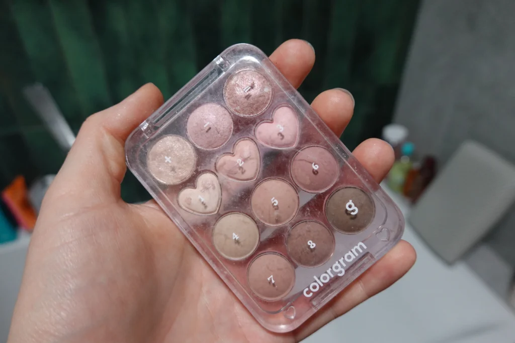 Colorgram Pin Point Eyeshadow Palette (02 Pink+Mauve) trzymana w kobiecej dłoni, w tle łazienka