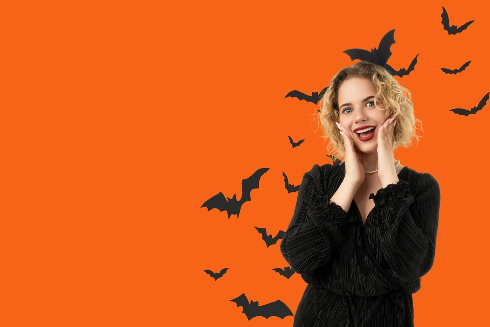 Kobieta w makijażu na pomarańczowym tle z nietoperzami, symbolami Halloween