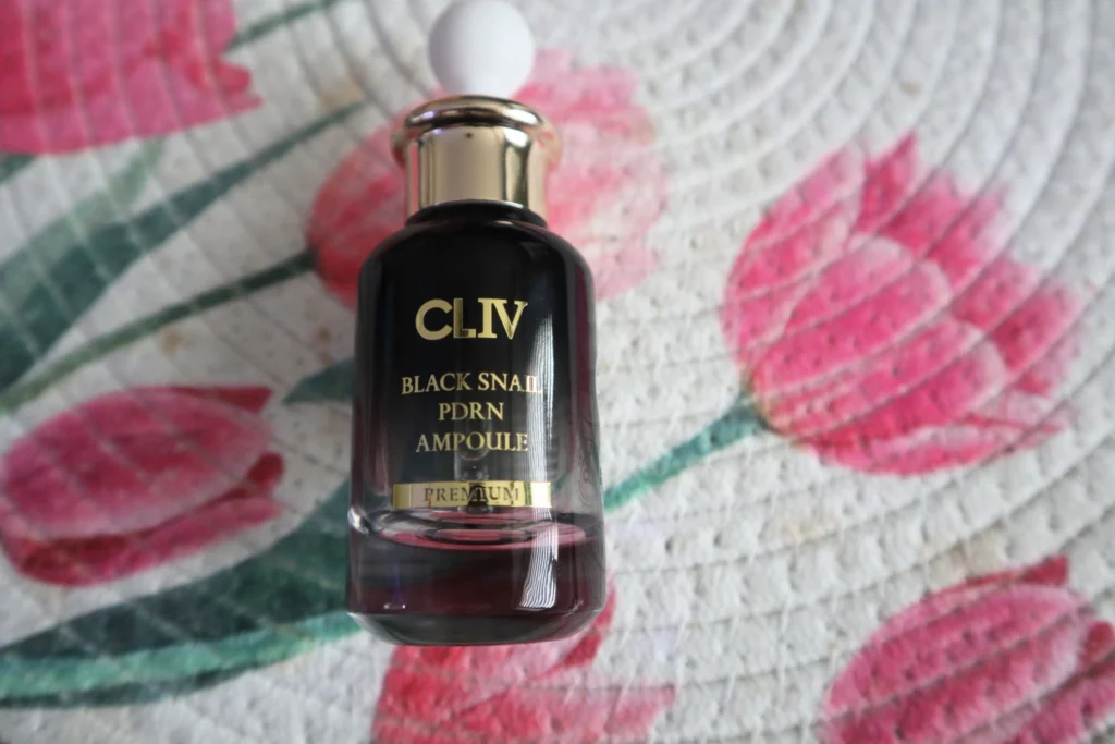 Zbliżenie na etykietę buteleczki CLIV Black Snail PDRN Ampoule Premium na tle tkaniny w różowe tulipany
