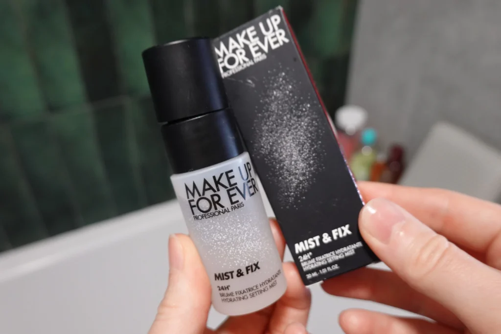 Make Up For Ever Mist & Fix Mini mgiełka utrwalająca pod makijaż trzymana w kobiecej dłoni w łazience